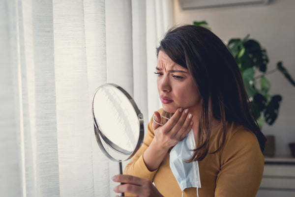 Worried woman with pimple looking in the mirror