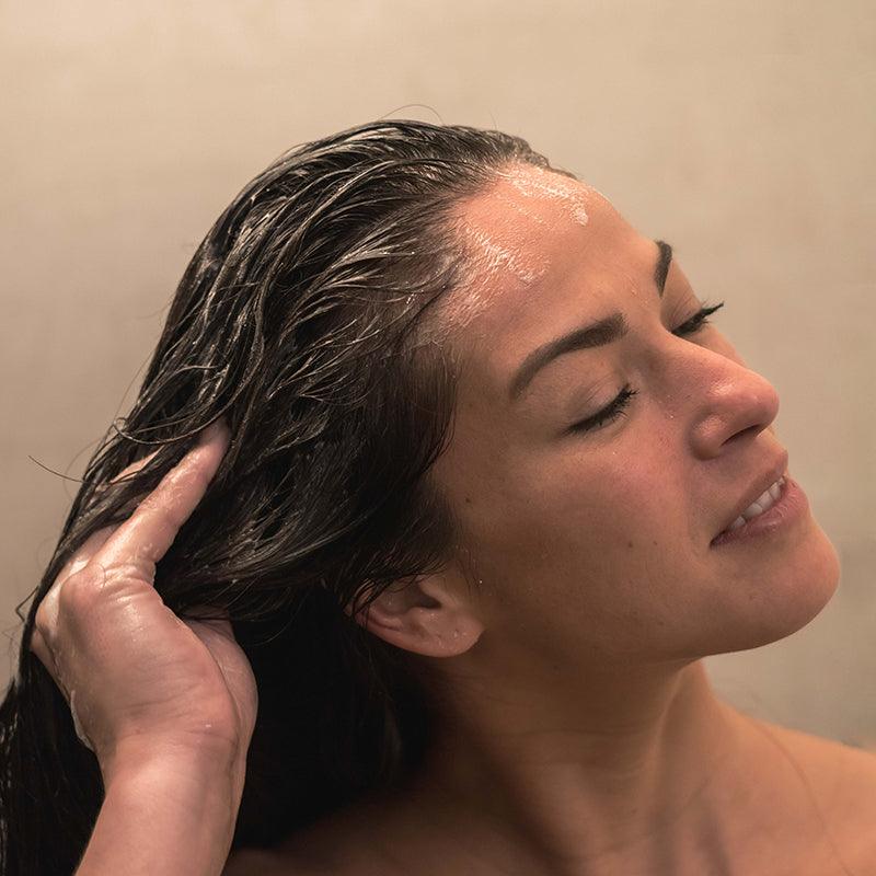 Woman showering with neofollics scalp exfoliating shampoo
